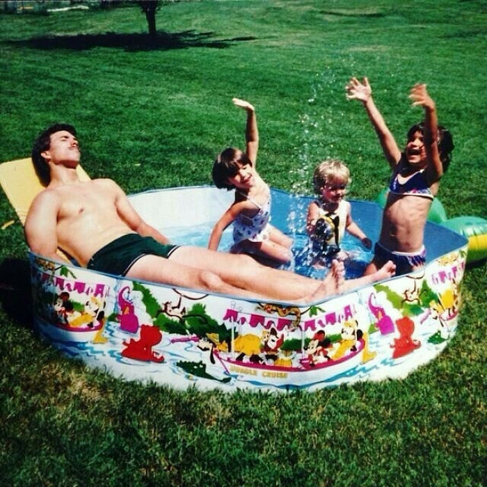 Dad and children enjoying a sunny day in a colorful kiddie pool, showcasing old school cool family fun outdoors.