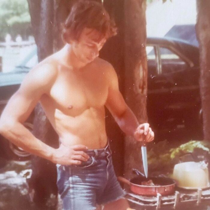 Shirtless dad cooking outdoors in denim shorts, embodying old school cool style from the past.