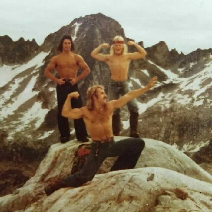 Three shirtless dads from the past posing on a rocky mountain, embodying old school cool with confident, muscular poses.