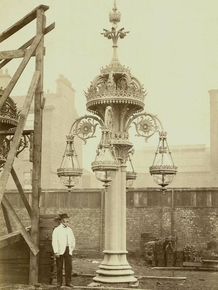 Man standing next to an ornate vintage street lamp showcasing old architecture from the past.
