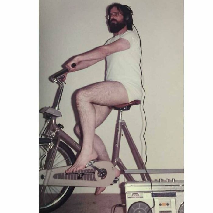 Vintage dad on stationary bike wearing headphones and shorts next to boombox, embodying old school cool style and vibe.