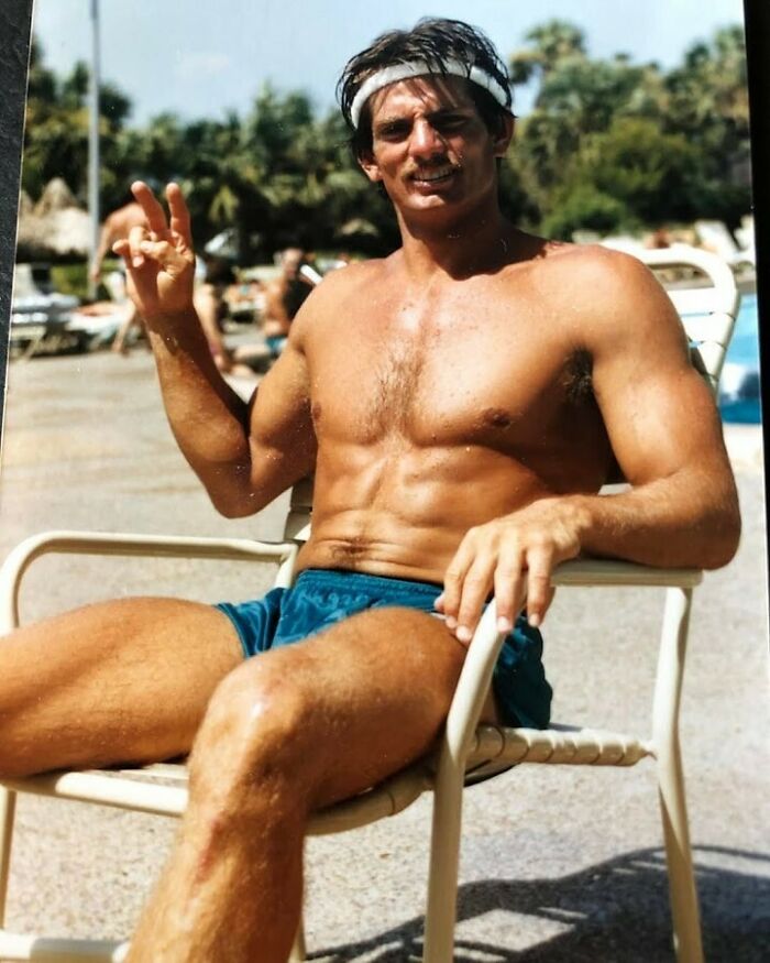 Vintage photo of a shirtless dad in blue shorts and headband relaxing poolside, radiating old school cool style and confidence.