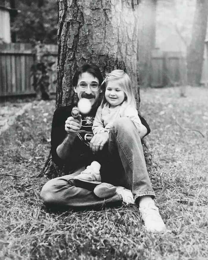 Black and white photo of a dad and daughter sitting by a tree, capturing old school cool dad vibes from the past.