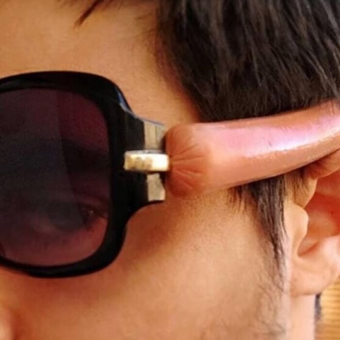 Close-up of a person wearing sunglasses with an arm made of a sausage, a funny picture that makes no sense.