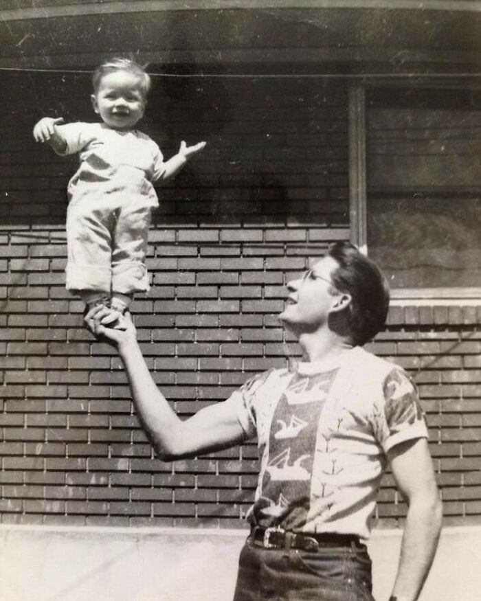 Vintage black and white photo of a dad balancing a baby on one hand, showcasing old school cool dads from the past.