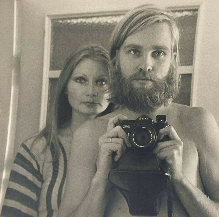 Vintage photo of a bearded dad holding a Canon camera with a woman behind him, showcasing old school cool style.