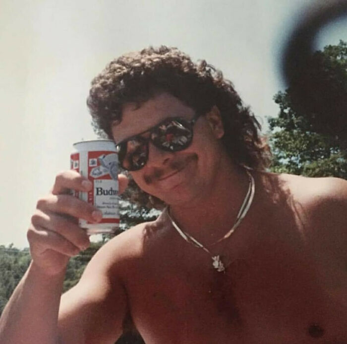 Man with curly hair and sunglasses raising a Budweiser can, embodying old school cool dads from the past.
