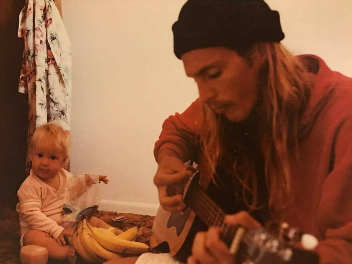 Vintage photo of an old school cool dad playing guitar with his child sitting nearby on the floor with bananas.