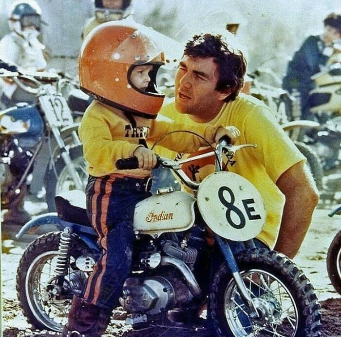 Young child on a vintage dirt bike with helmet, guided by dad, showcasing old school cool dads bonding outdoors.