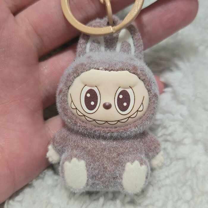 Hand holding a creepy fuzzy Labubus keychain with exaggerated eyes and a wide grin, resembling a fake toy.
