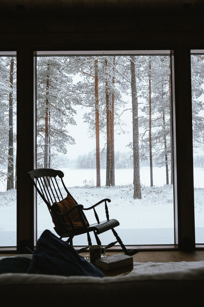 Cozy cabin interior with rocking chair facing snowy woods, showcasing peaceful cabin in the woods retreat and nature views. - 10