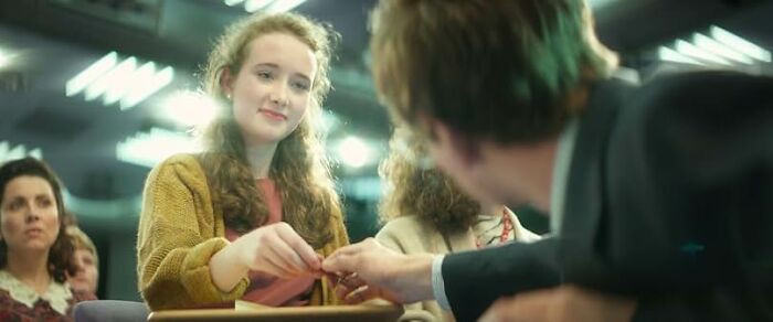 Young woman in a cozy sweater handing an item to a man in a suit during a friendly gathering, worst movie tropes quiz theme.