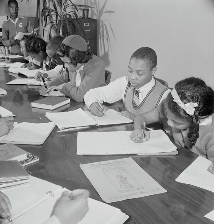 Students studying and writing at a table in a classroom, captured in a historic school image from World War II.