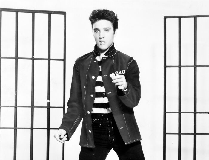 Young man in striped prison uniform holding a number tag, symbolizing a journey from poverty to super wealthy.