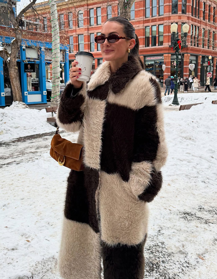Influencer wearing a fur coat and sunglasses outdoors in snowy city, drinking coffee, amid backlash for buying toilet paper.