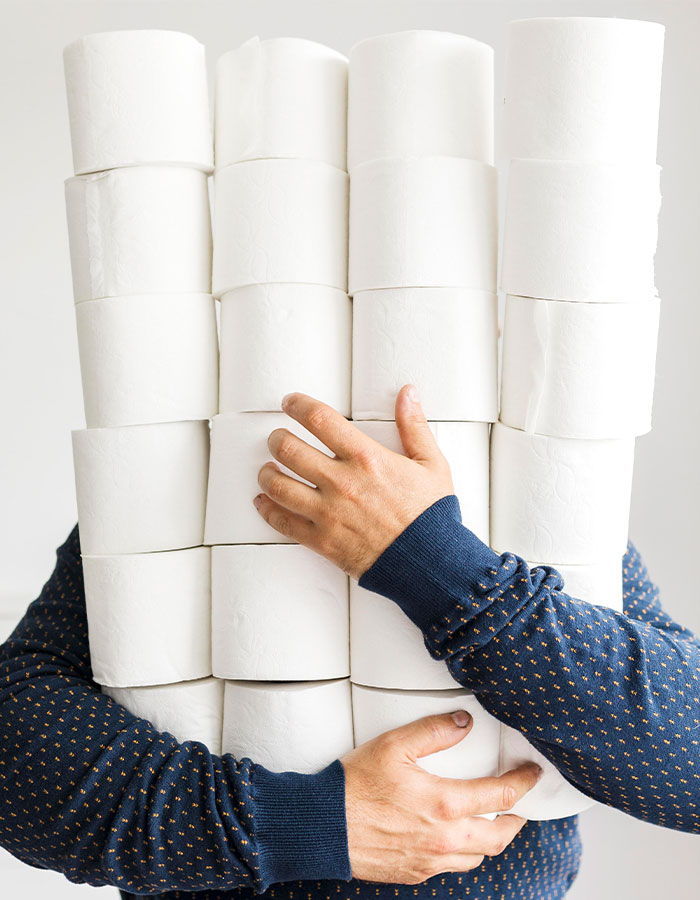 Person wearing a blue sweater holding a large stack of toilet paper rolls tightly against a plain white background