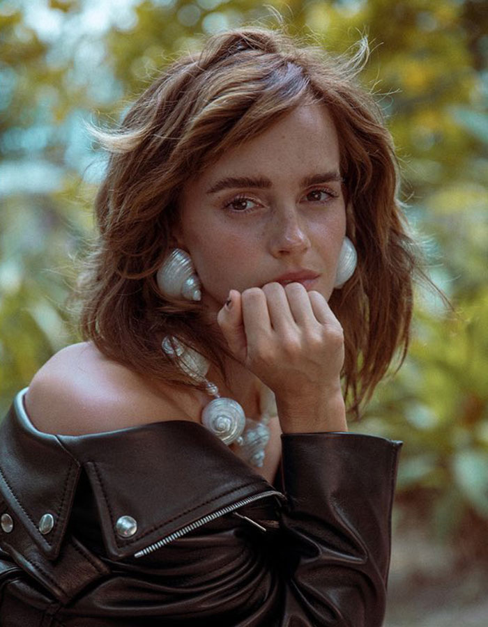 Emma Watson in a contemplative pose wearing a black leather jacket and large shell-themed jewelry outdoors in soft natural light. - 8
