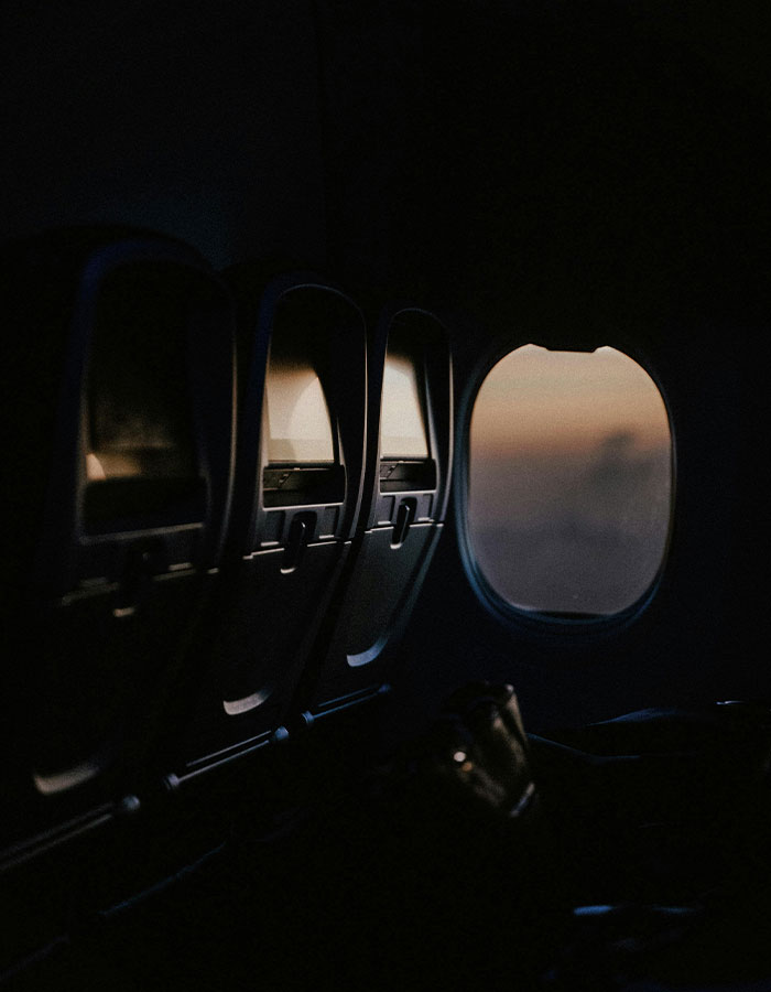Dimly lit airplane cabin seats with window showing sunset, illustrating passenger fumes over disrespectful PDA act on plane.