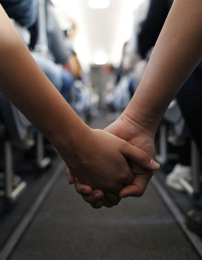 Two passengers holding hands on a plane aisle, highlighting PDA act causing passenger fumes and heated debate. - 6