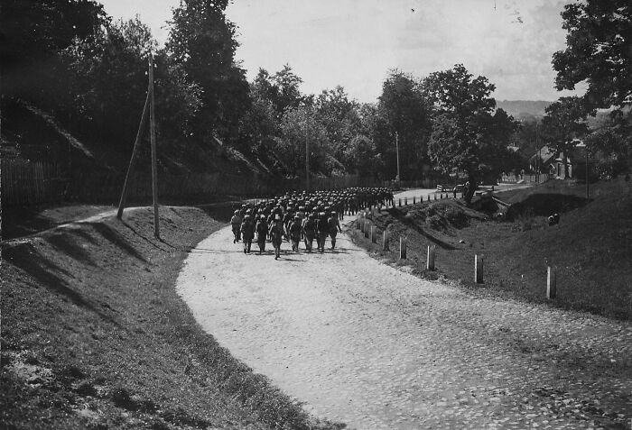 Historical photographs showing a group of soldiers marching on a rural road surrounded by trees and fences.