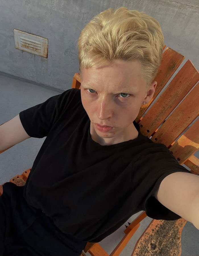 Model with short blonde hair sitting in an orange chair, reflecting on transitioning and detransitioning experience. - 3