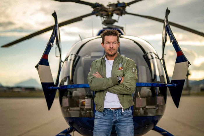 Man standing confidently in front of a helicopter, representing daredevil skydiver viral final moments. Man standing confidently in front of a helicopter, representing daredevil skydiver viral final moments.