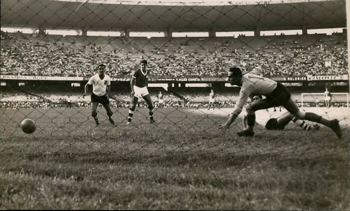 1950s daily life photo showing a vintage soccer match with players and goalkeeper in action on the field.