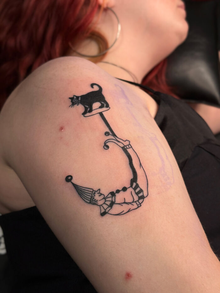 Black ink tattoo of a playful clown holding a black cat on the upper arm, one of the best tattoos liked by many.