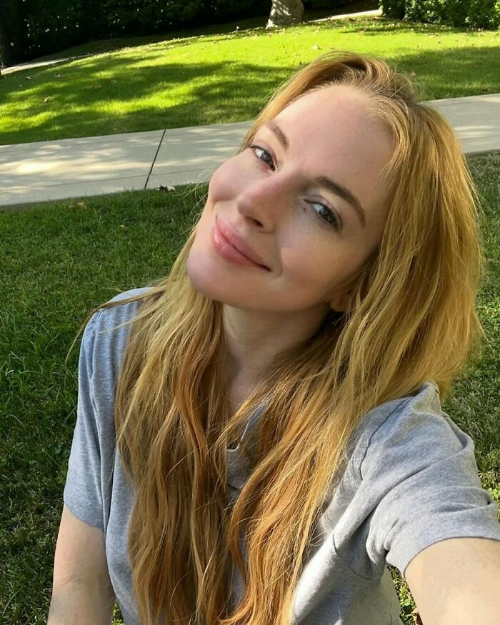 Lindsay Lohan smiling outdoors showing fresh-faced glow amid plastic surgery drama, looking 10 years younger in natural light.