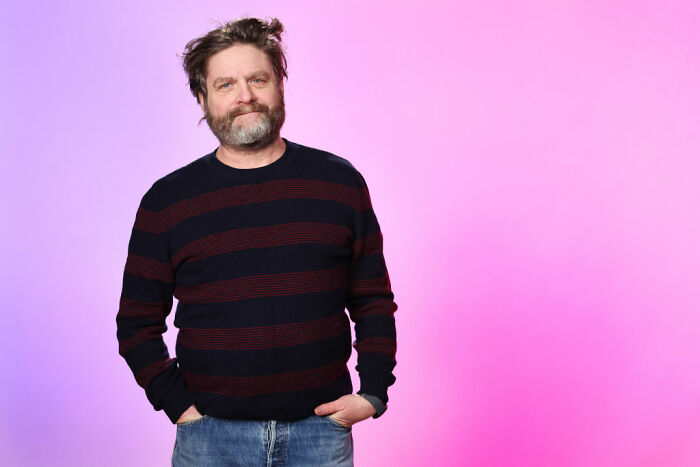 Bearded man in a casual striped sweater and jeans posing confidently, representing celebrities who choose not to overspend.
