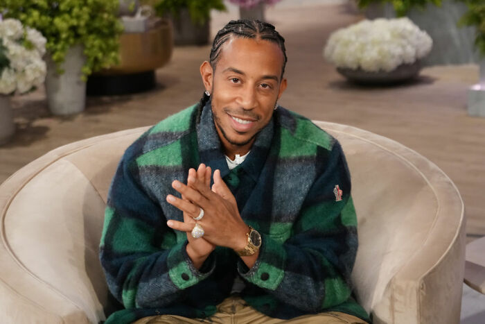 Celebrity wearing a green and navy plaid jacket sitting and smiling, representing celebrities who avoid overspending.