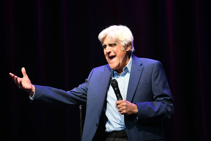 Older male celebrity in blue suit speaking on stage with microphone, example of celebrities who avoid overspending despite wealth