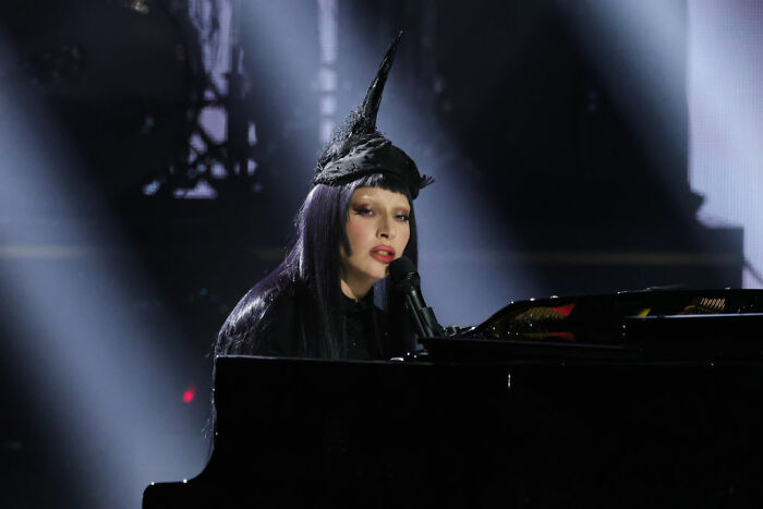 Celebrity wearing a unique black hat performing on piano under spotlight, reflecting modest luxury of celebrities who avoid overspending.