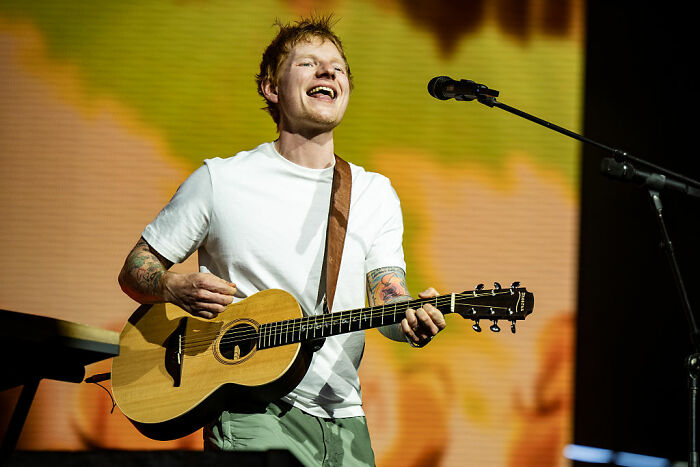 Male musician playing acoustic guitar and singing on stage, representing celebrities that choose not to overspend.