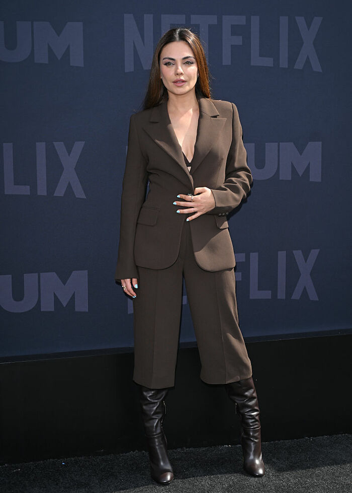 Celebrity in a brown suit and black boots posing at a Netflix event, exemplifying modest luxury among wealthy celebrities.
