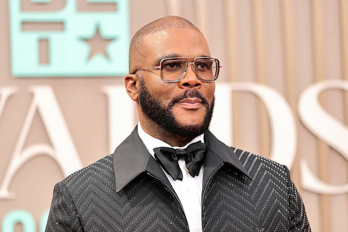 Tyler Perry at an awards event wearing glasses and a stylish black suit, representing celebrities who choose not to overspend.
