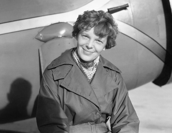 Amelia Earhart smiling in front of an airplane, related to the Amelia Earhart mystery and new satellite clues.