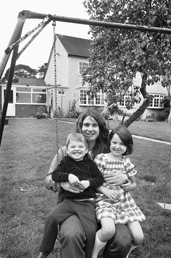Ozzy Osbourne with two kids on a swing in a garden, reflecting family moments amid reported deep family rifts.