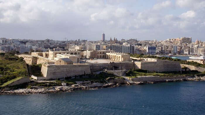 Historic building near water with stone fortifications and cityscape in the background, representing saved historic architecture.