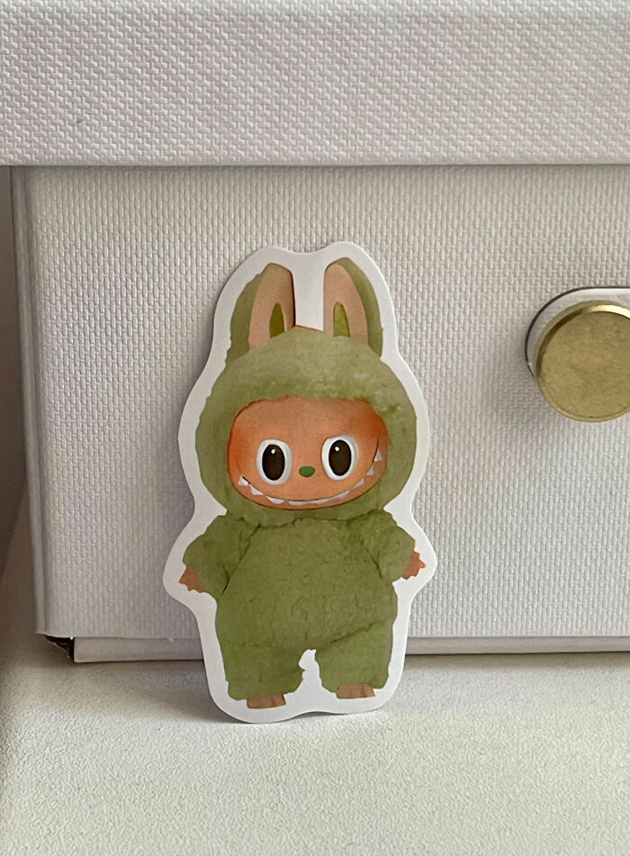 Sticker of a small character in a green bunny costume placed against a white textured surface, showing presence before it was cool.