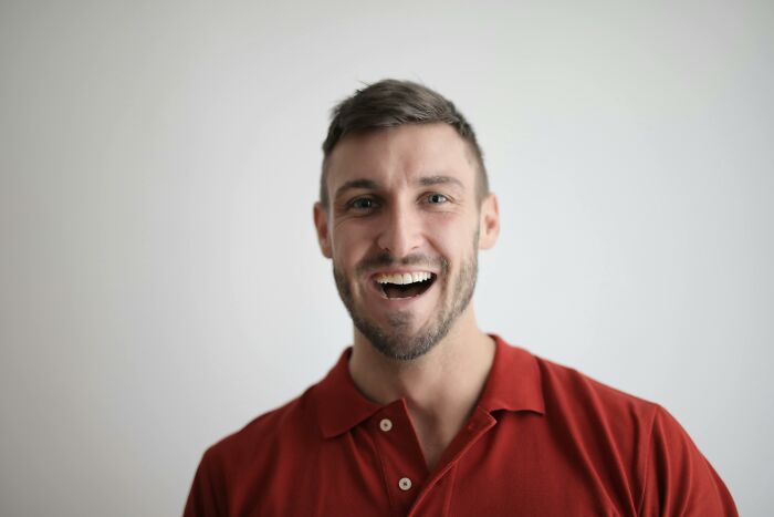Smiling young man in a red shirt looking at the camera in a bright room, expressing joy and openness for how would you call them.