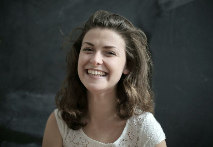 Young woman smiling warmly with wavy hair against a dark background, representing how would you call them concept.