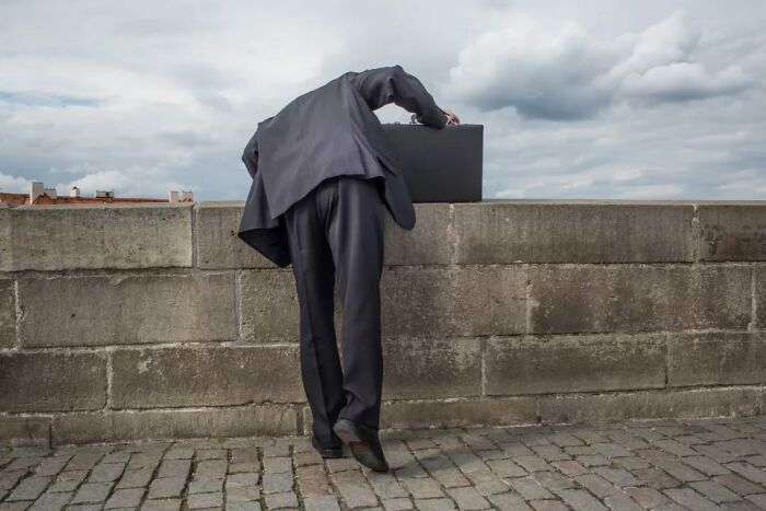 Man in suit leaning over wall with briefcase in hand, a serendipitous moment captured in everyday street photography.
