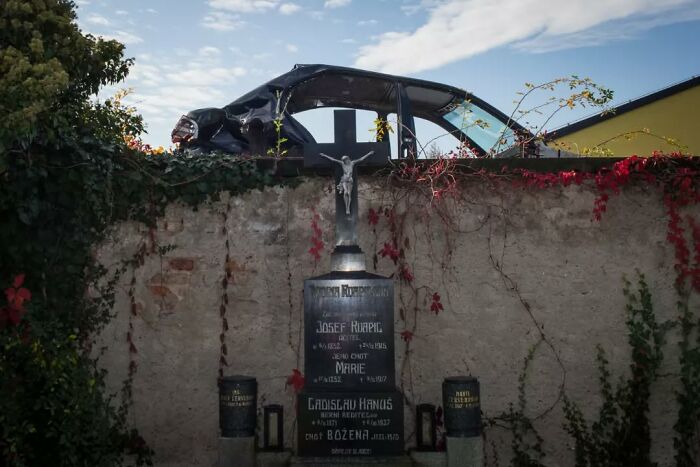 Abandoned car and weathered tombstone with crucifix captured in a street photographer’s serendipitous everyday moment.
