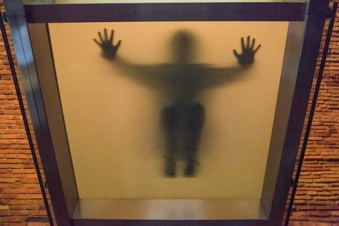 Shadowy figure pressed against frosted glass with hands spread, creating a fun accidental moment captured by a street photographer.