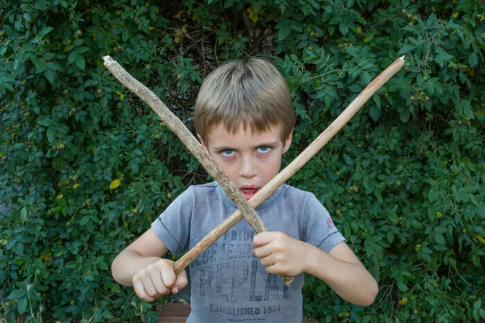 Young boy holding two sticks crossed in front of him, capturing a serendipitous moment in everyday life by a street photographer.