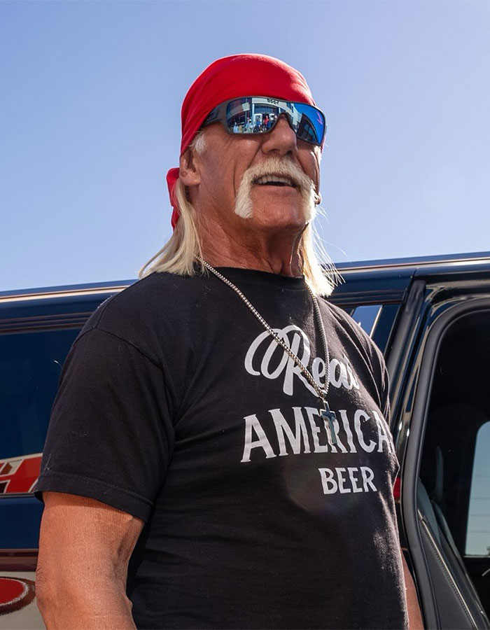 Hulk Hogan wearing a red bandana and sunglasses outside by a vehicle amid groveling apology backlash.
