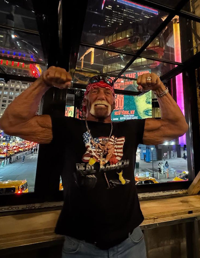 WWE legend Hulk Hogan flexing muscles indoors at night with city lights and billboards in the background. - 6