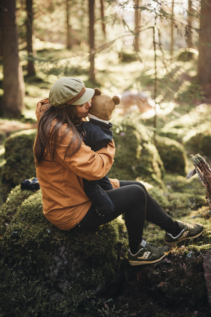 Woman sitting on mossy rock in the woods, holding a child, enjoying peaceful cabin life in nature’s quiet embrace. - 17