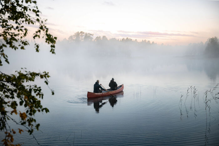 Two people paddling a canoe on a misty lake near a cabin in the woods, embracing peaceful nature and solitude. - 11